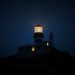 Faro encendido de noche sobre un acantilado oscuro