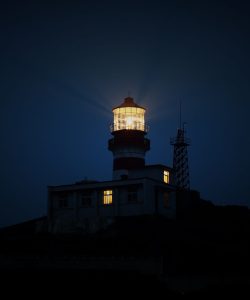Faro encendido de noche sobre un acantilado oscuro