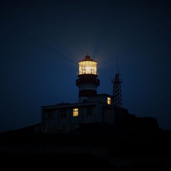 Faro encendido de noche sobre un acantilado oscuro